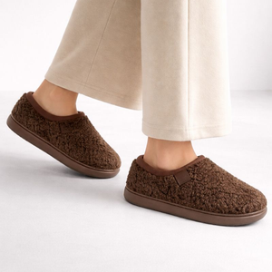 Brown slippers worn with beige pants on a white background