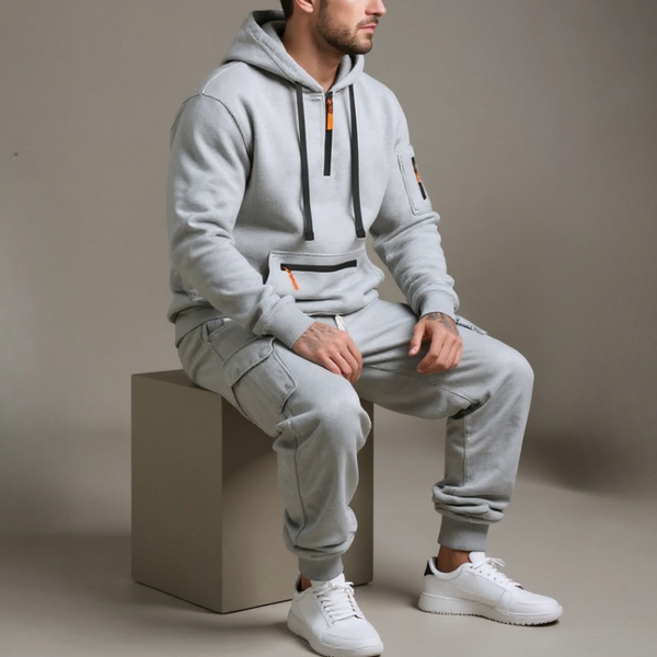 Person wearing a gray tracksuit sitting on a block with a neutral background