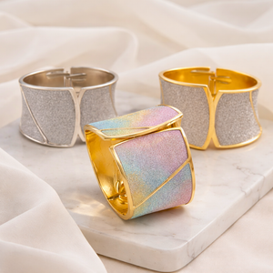 Three metallic cuff bracelets on a marble surface with a soft fabric background