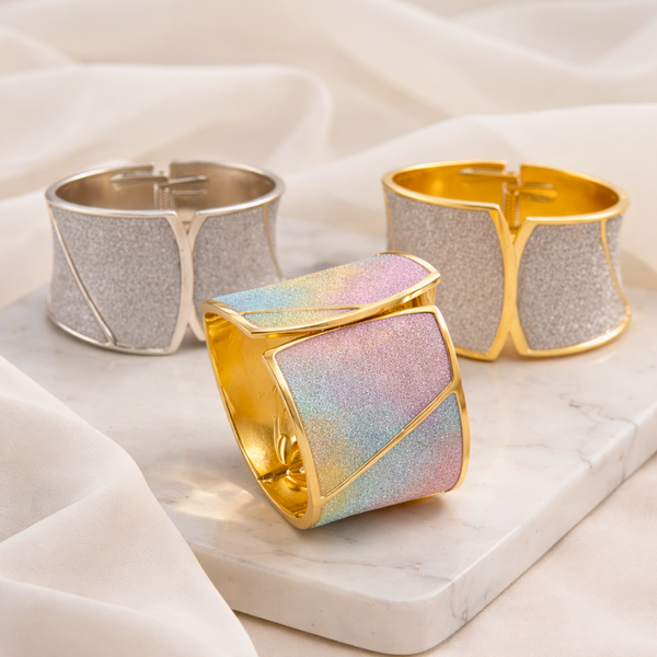 Three metallic cuff bracelets on a marble surface with a soft fabric background