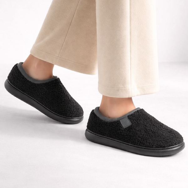 Black slippers worn with beige pants on a white background