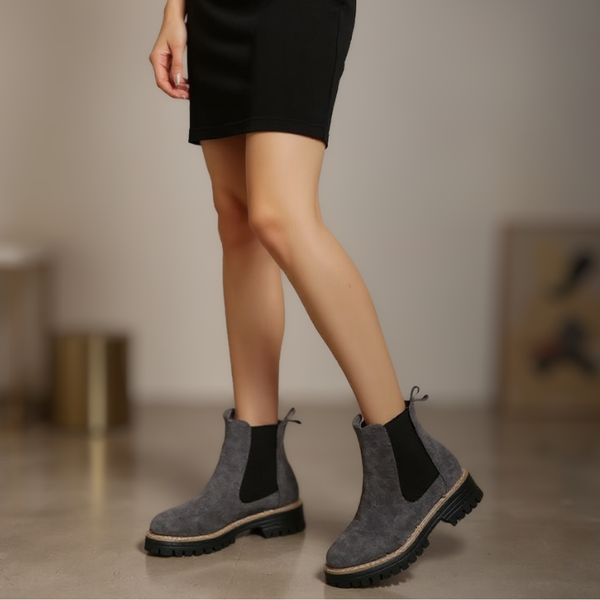 Person wearing gray Chelsea boots with black socks on a neutral background