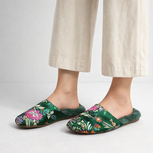Green floral slippers worn with beige pants on a light gray background