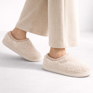 Beige slippers worn with light-colored pants on a white background