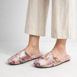Floral patterned slippers worn with light-colored pants on a neutral background
