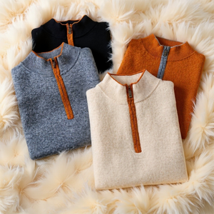 Four folded sweaters in blue, black, beige, and brown on a fluffy white surface.
