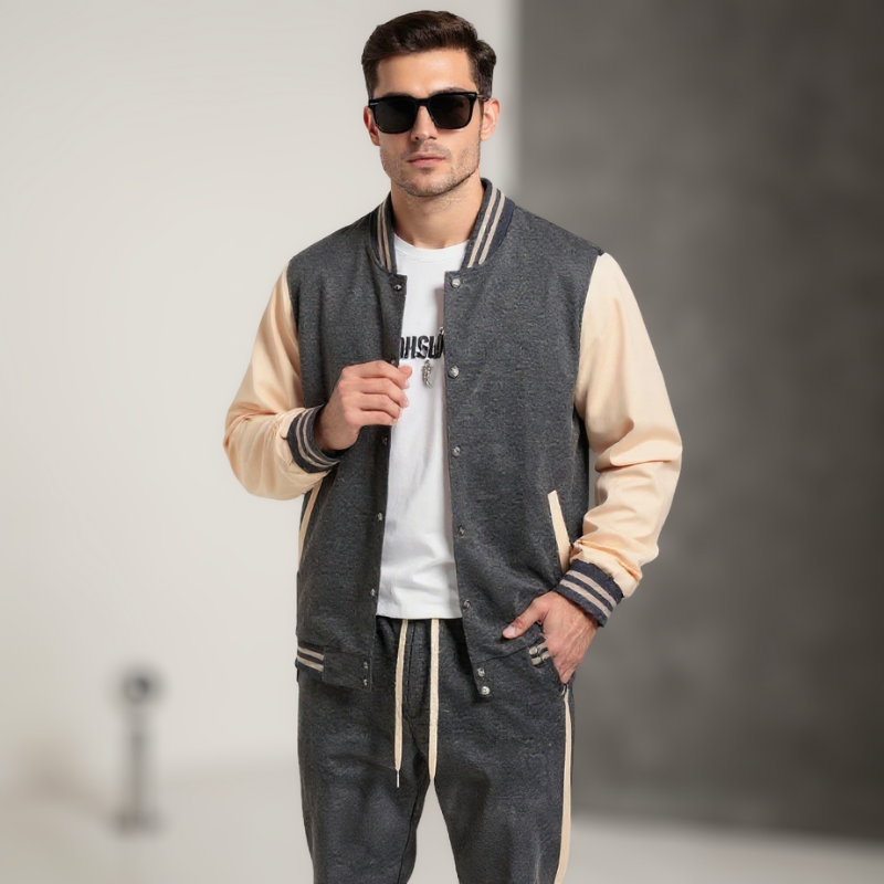 Man wearing a blue and beige varsity jacket with matching pants on a gray background