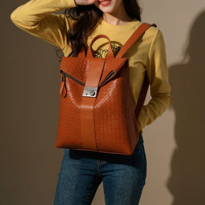 Person wearing a yellow long-sleeve shirt and blue jeans, holding an orange leather backpack against a plain background.