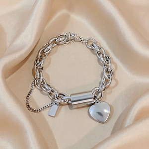 Silver chain bracelet with a heart-shaped tag on a beige fabric background