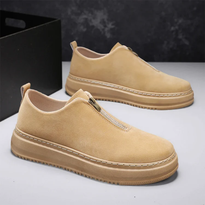 Black slip-on shoe with beige sole on a wooden surface with autumn leaves and a lake in the background