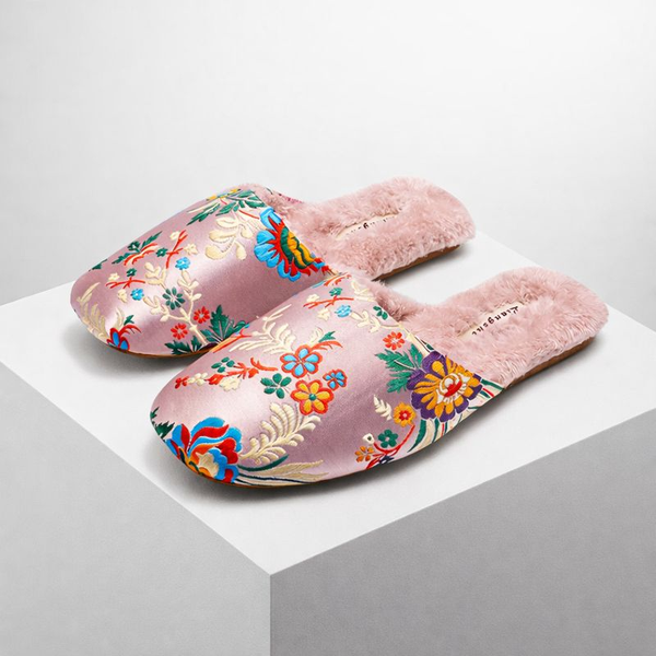 Pair of pink slippers with floral embroidery on a light gray background