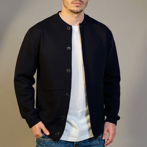 Man wearing a black varsity jacket over a white shirt with a plain background