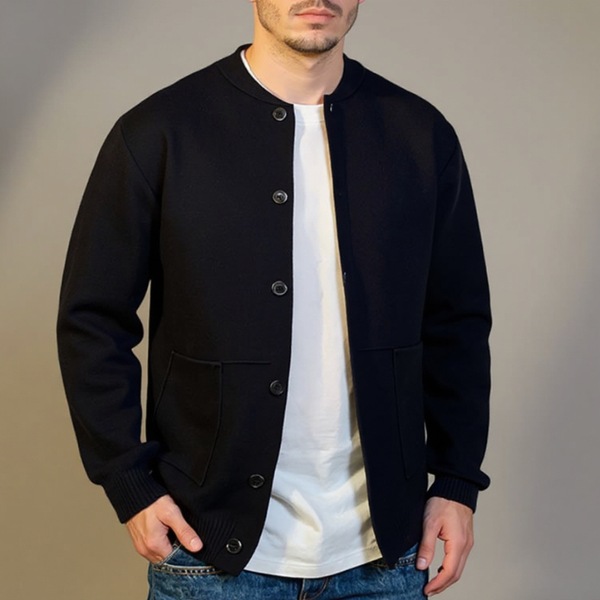 Man wearing a black varsity jacket over a white shirt with a plain background