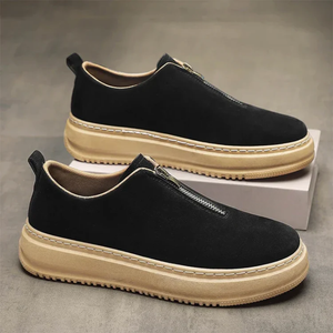 Black slip-on shoes with beige soles on a gray surface