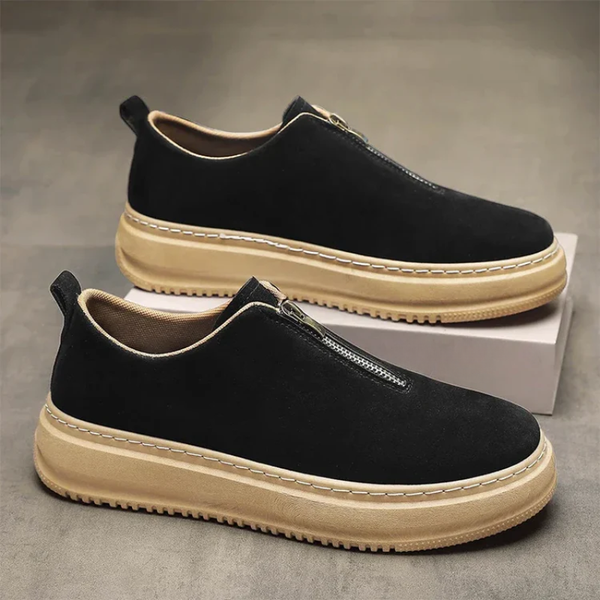 Black slip-on shoes with beige soles on a gray surface