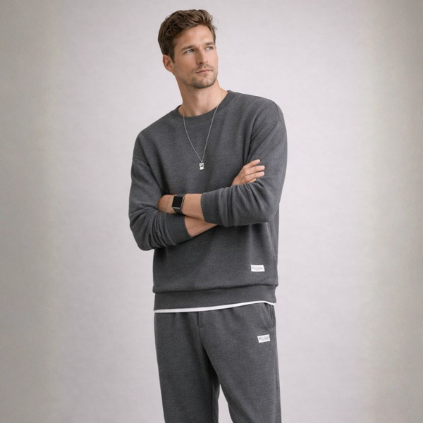 Man wearing a gray sweatshirt and pants with a plain background