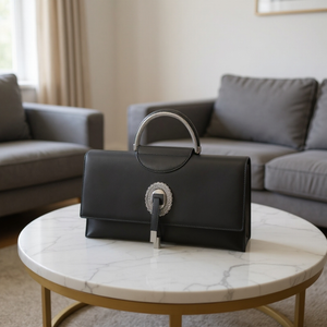 Black handbag with a decorative clasp on a marble coffee table in a living room.