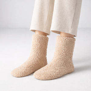 Beige fuzzy socks worn with light-colored pants on a plain background