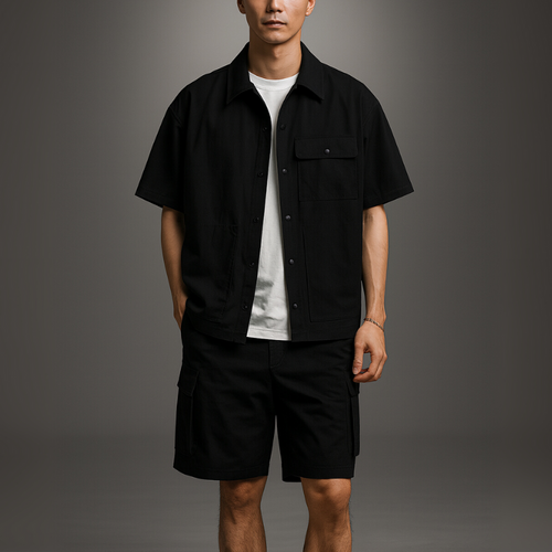 Man wearing a black short-sleeve shirt over a white t-shirt and black shorts on a gray background