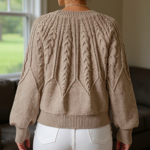 Person wearing a beige cable knit sweater in a room with a window in the background