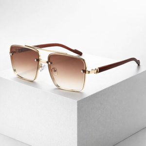 Sunglasses with gold frame and brown gradient lenses on a light gray surface