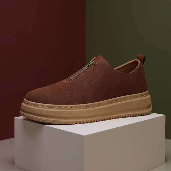 Brown slip-on shoe with a thick sole on a white block against a gradient background