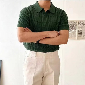 Person wearing a green textured shirt and beige pants with arms crossed, standing against a light background.