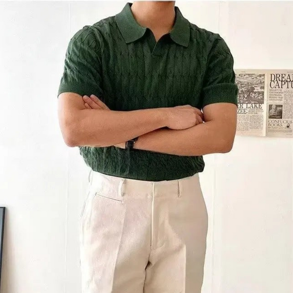 Person wearing a green textured shirt and beige pants with arms crossed, standing against a light background.