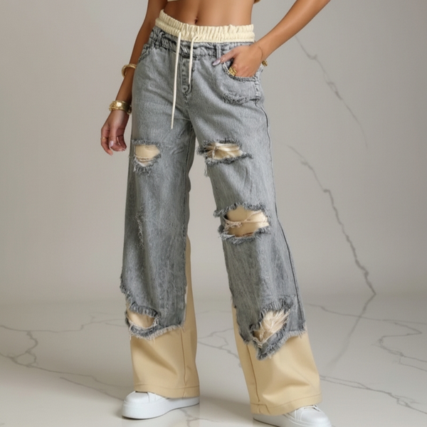 Person wearing ripped jeans with beige accents on a neutral background