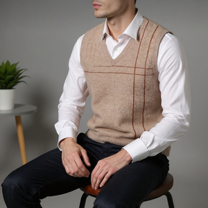 Man wearing a beige sweater vest over a white shirt, sitting on a stool against a gray background.