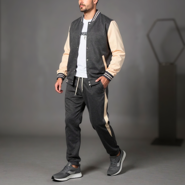 Man wearing a gray and beige varsity jacket with black pants on a gray background