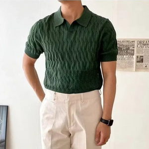 Person wearing a green textured polo shirt and beige pants against a white wall.