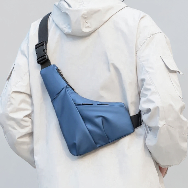 Person wearing a blue sling bag over a light-colored jacket on a plain background