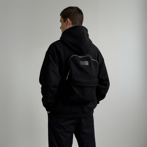 Person wearing a black hoodie with a logo on the back against a plain background
