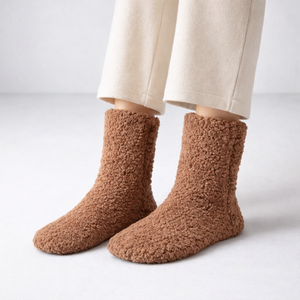 Brown fuzzy socks worn with beige pants on a light gray background