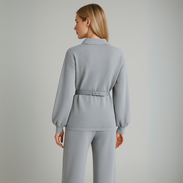 Woman wearing a light gray outfit with a belt against a plain background