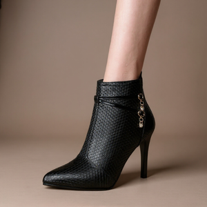 Black high-heeled ankle boot with decorative chain on a beige background