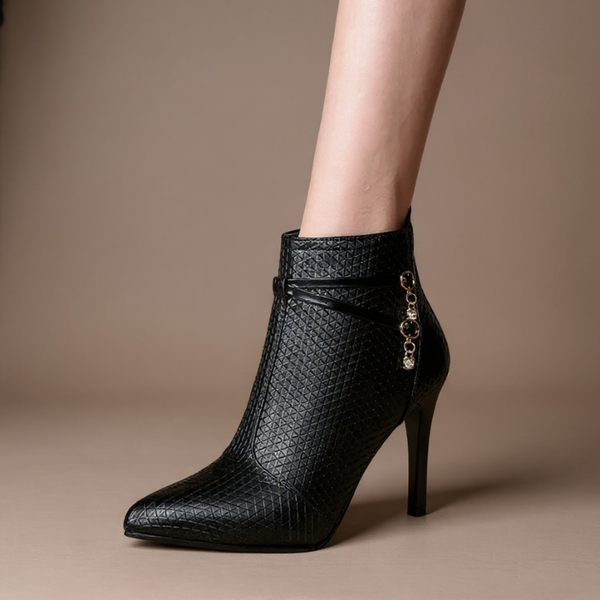 Black high-heeled ankle boot with decorative chain on a beige background