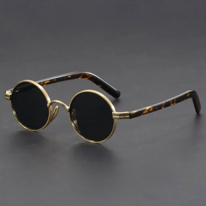 Round sunglasses with gold frame and tortoiseshell accents on a dark background