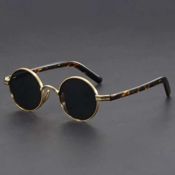 Round sunglasses with gold frame and tortoiseshell accents on a dark background