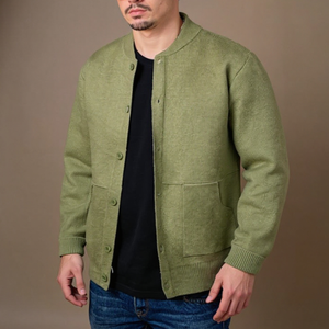 Man wearing a green cardigan over a black shirt with a brown background