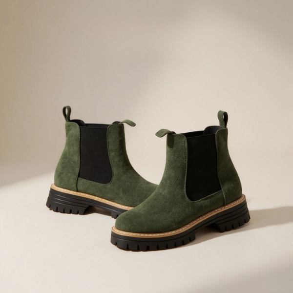 Pair of green suede Chelsea boots on a beige background