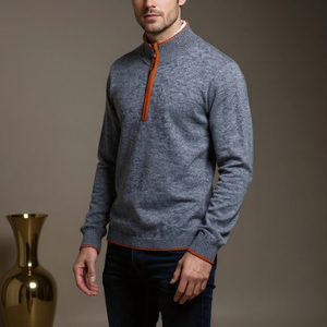 Man wearing a gray sweater with orange accents standing next to a gold vase on a brown background