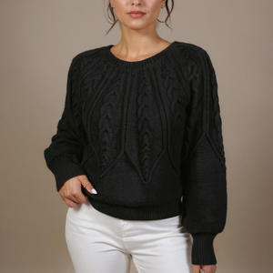 Person wearing a black cable knit sweater and white pants on a beige background
