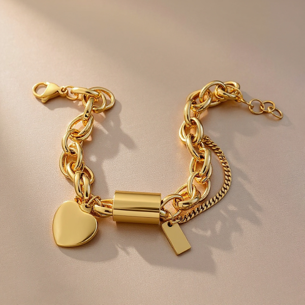 Gold chain bracelet with heart and cylindrical lock charm on a beige background