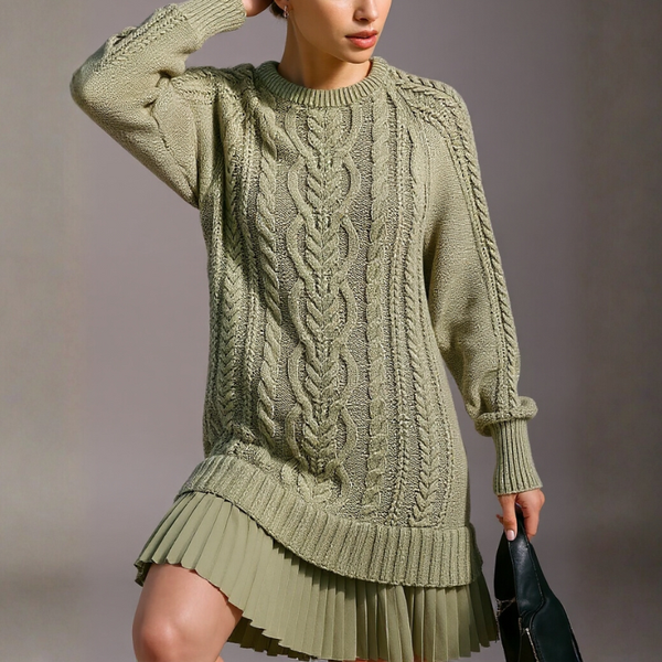 Person wearing a green cable knit sweater and pleated skirt against a neutral background