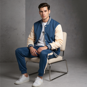 Man sitting on a chair wearing a blue and beige varsity jacket with matching pants.