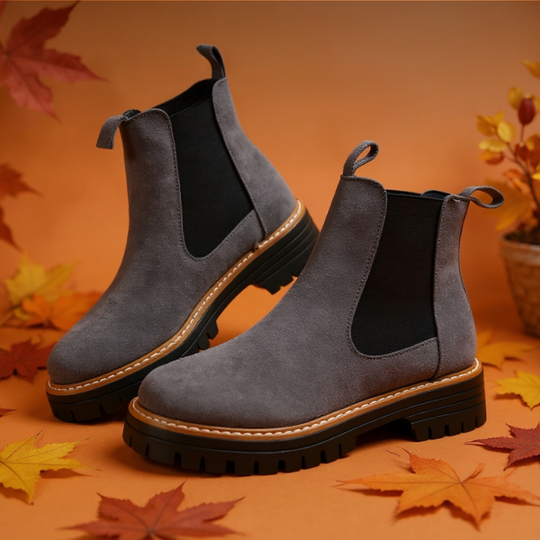 Gray suede boots with black soles on an orange background with autumn leaves.