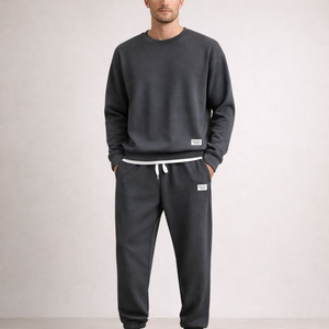 Person wearing a dark gray sweatshirt and pants set on a plain background