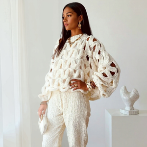 Woman wearing a white textured sweater and pants in a minimalistic setting.